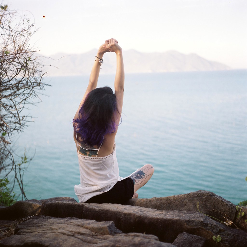 Woman stretching her arms overhead while sitting on rocks by a calm lake