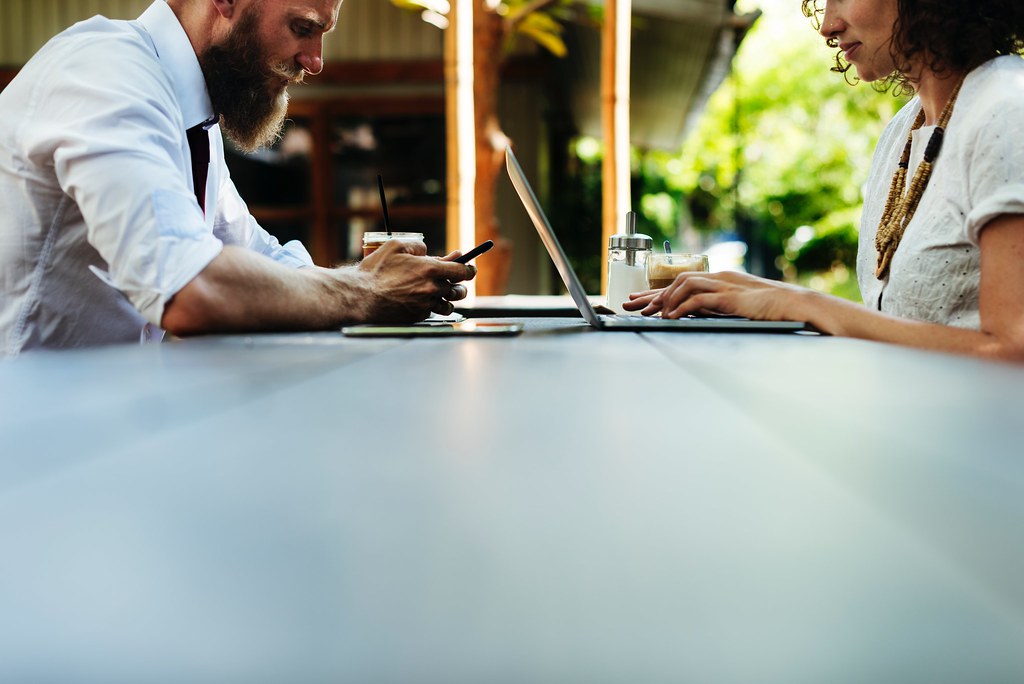 Two people working on laptops at a long table in a bright office